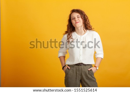 Portrait of a stylish squinting girl standing isolated on yellow background.