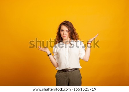 beautiful young girl chooses two items standing isolated on yellow background