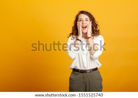 beautiful young girl surprised with open mouth holds hands on cheeks isolated on yellow background