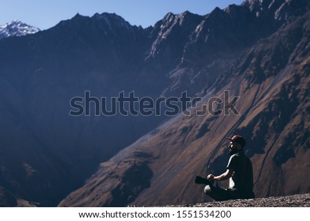 stylish bearded man with camera in hands on top of Georgian mountains: nature photographer traveler taking photo of beautiful landscape from top of the mountain