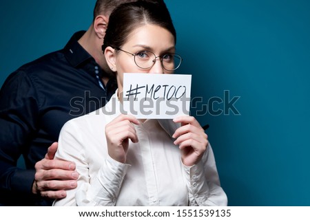 an office employee covers her mouth with a sign with an inscription metoo, and behind her you can see the silhouette of a man