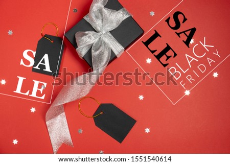 Black friday sale concept. Black paper boxes with silver ribbon, price tags, stars confetti and text on bright red background. Flat lay, top view, copy space