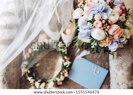 Delicate bouquet with peonies. Wedding accessories of the bride. Elegant wedding bouquet with ribbon, wedding invitations, engagement rings and shoes for the bride on a chair. selective focus.