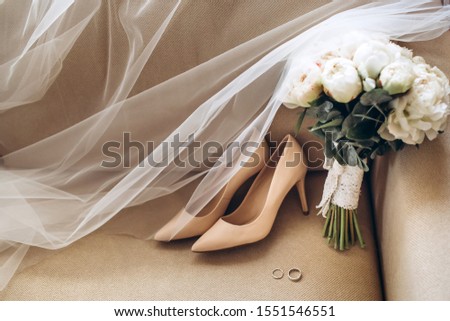 Wedding shoes of the bride with a bouquet of peonies and other flowers on the armchair. Tender morning of the bride. Stylish wedding accessories of the bride.