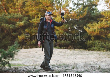 Male hiker making photo and video of beautiful locations with stabilizer for mobile phone. Smartphone attached to a gimbal. Forest on background.