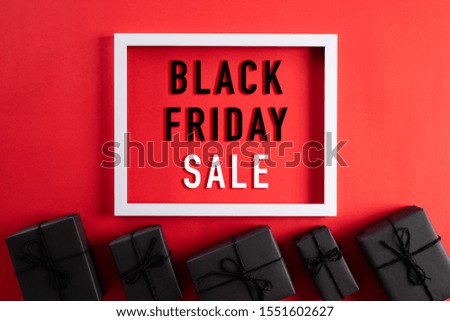 Top view of Black Friday Sale text on white picture frame with black gift box and Christmas ball and berries on red background. Shopping concept and black Friday composition.