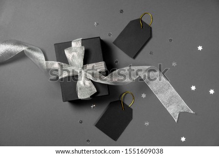 Gift box wrapped in black paper with silver ribbon, stars confetti and price tags on gray background. Copy space and top view. Black friday box gift present isolated.