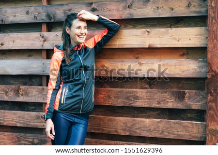 Lifestyle portrait of a laughing caucasian young sportswoman against a wooden wall outside. Copy space.