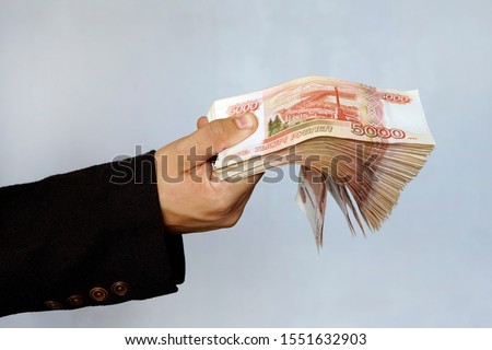 Hand with Russian rubles on a blue background, bills five thousand rubles, money fan in hand. a large wad of money with a million rubles in the hand of a successful young man. Royalty-Free Stock Photo #1551632903