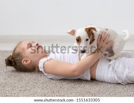people, children and pets concept - little kid girl lying on the floor with cute puppy in hands