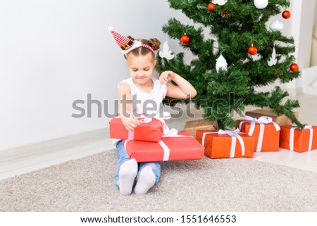 Kid opening Xmas presents. Child under Christmas tree with gift boxes.