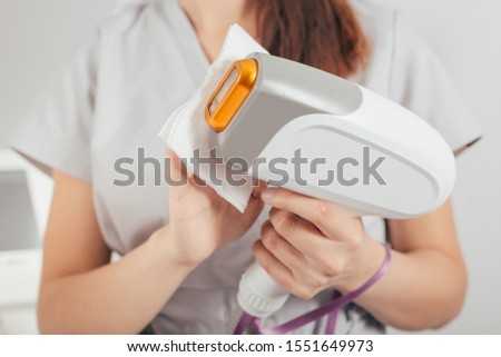 A woman tunes a laser hair removal machine. She holds a working part of the epilator in her hands and poses for a photo. It is located in a modern beauty salon. Body Care. Underarm Laser Hair Removal.
