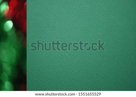 Textured green paper with a stripe of Christmas bokeh. Red with green bokeh on the left side. Macro. Blank for business card, menu design, congratulations. Flat lay, close up, copy space