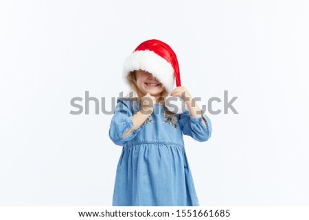 Happy smiling child girl in Santa hat and blue dress having fun on a red isolated background. Merry Christmas. Happy New Year