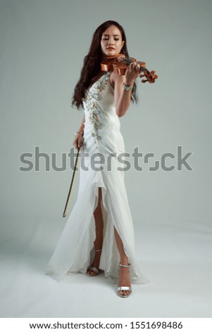 Southeast Asian violinist, Young beautiful Asian woman playing violin on gray background.