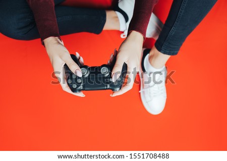 Young thin woman playing with black gamepad, sitting on red background. flat lay.