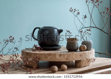 Stylish autumn composition of home decor on living room with wooden fruit tray, cement fruits, tea jug  and autumn flowers. Eucalyptus color concpet. Template. Modern decoration. Close up. 