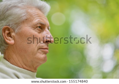 Serious senior man looking in park on green background