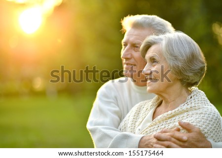 Happy elderly couple at nature on leaves and sunset background