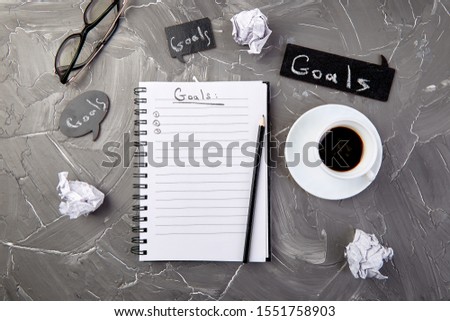 Goals as memo on notebook with idea, crumpled paper, cup of coffee over on grey background. Top view.