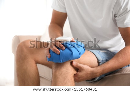 Man applying ice pack on knee at home, closeup. Health problems Royalty-Free Stock Photo #1551768431