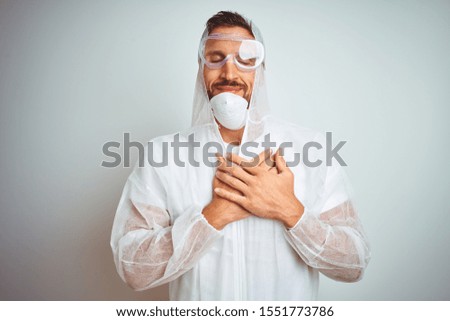 Painter man wearing professional worker equipment protection over isolated background smiling with hands on chest with closed eyes and grateful gesture on face. Health concept.