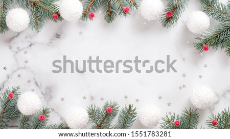 Christmas frame with fir tree branches, white balls, red berries and confetti on marble background. Flat lay, top view, overhead