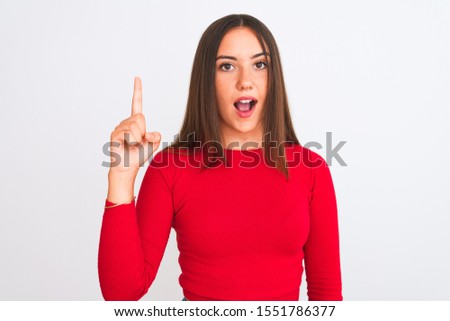 Young beautiful girl wearing red casual t-shirt standing over isolated white background pointing finger up with successful idea. Exited and happy. Number one.