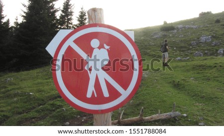 Red hiking ban sign in front of green meadow