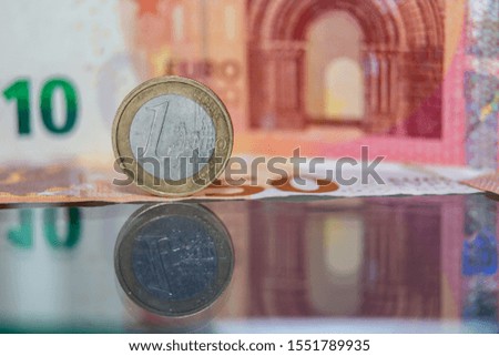 Macro photo of a coin in 1 euro on a blurred background banknote in ten euro. Reflection of the coin on the glass table. Very small depth of field.