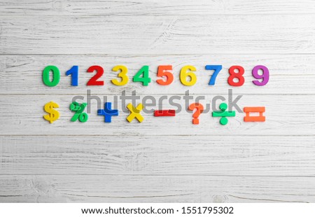 Colorful magnetic numbers and math symbols on white wooden background, flat lay