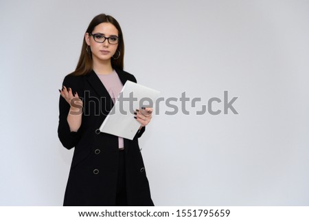 Close-up portrait of a young pretty girl secretary with long black hair in a black business suit, on a white background. Standing right in front of the camera in different poses with emotions.