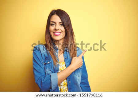 Young beautiful woman standing over yellow isolated background cheerful with a smile on face pointing with hand and finger up to the side with happy and natural expression