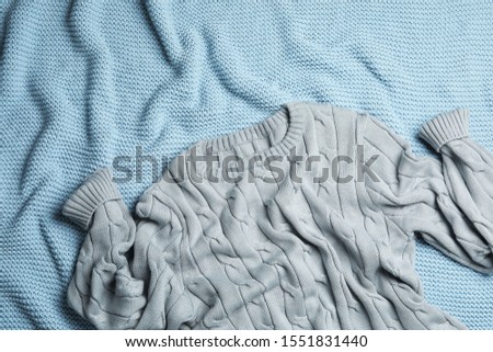 Warm grey knitted sweater on light blue blanket, flat lay