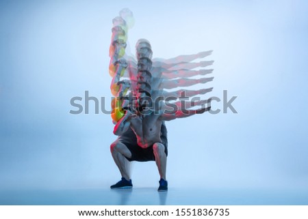 Balance. Young caucasian bodybuilder training over studio background in neon and strobe light. Muscular male model with the weight. Concept of sport, bodybuilding, healthy lifestyle, motion and action
