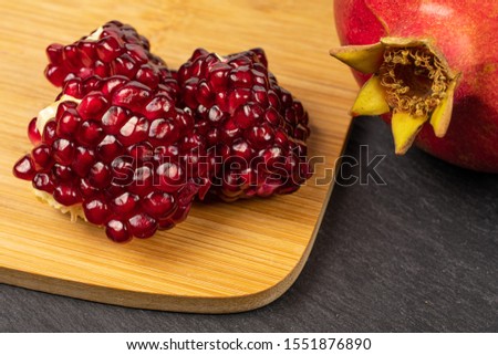 Group of one whole three pieces of fresh red pomegranate on bamboo cutting board on grey stone