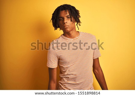 Afro man with dreadlocks wearing striped t-shirt standing over isolated yellow background looking sleepy and tired, exhausted for fatigue and hangover, lazy eyes in the morning.