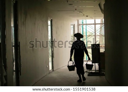 The silhouette of a worker carrying a cement bucket walking to put the cement to plaster on the interior of the building