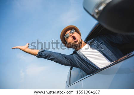 An Asian man is enjoying his trip. He stretches out of the car window to make him look happy.
