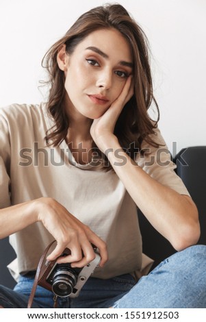 Picture of beautiful young woman photographer on sofa indoors at home holding camera.