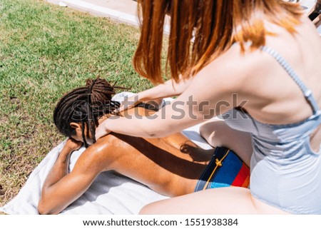 Stock photo of a black boy with dreadlocks lying on the grass while a girl does a massage. Summertime