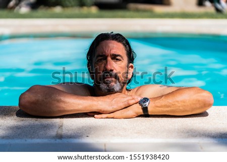 Stock photo of a Man leaning his arms on the edge of a pool with wet hair and wearing a watch. Summertime and leisure