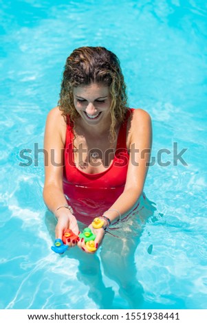 Vertical stock photo of a blonde girl with a red swimsuit inside the pool with rubber ducks in her hands. Holidays and games