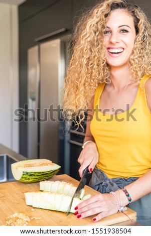 Vertical stock photo of a girl cutting melon and looking at the camera with a smile. Holidays and food