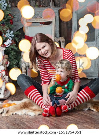 Portrait of happy mother and adorable baby celebrate Christmas. New Year's holidays. Baby boy with mom in the decorated room with Christmas tree and decorations.