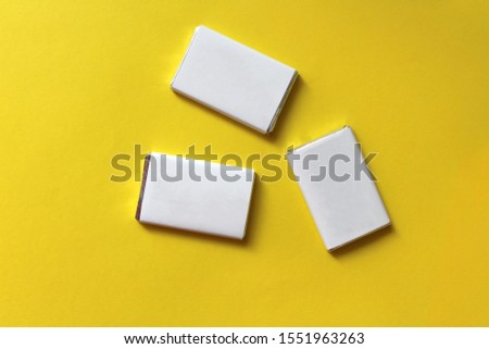 Chocolates wrapped in silver foil and white blank paper. Copy space for text. Template for greeting card, poster or invitation. Sweet candies scattered on yellow smooth table. Backdrop or background
