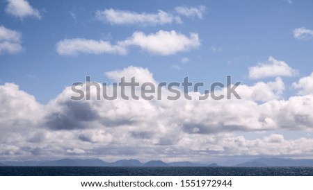 A seascape, looking from a distance at the North sea coast of Norway, with dark mountains in the background and a dramatic cloudy sky hanging over the water.