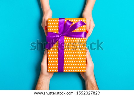 Top view of a man and a woman holding a gift box on colorful background. Love and relationship concept. Close up.
