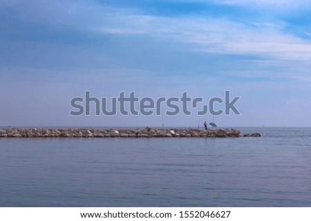 A man catches a fish on fishing rods on a stone breakwater on a summer evening. Malaga, Spain