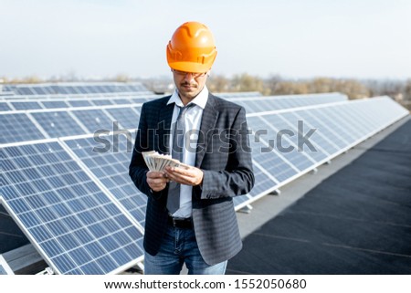 Portrait of a happy businessman with money earned from the electricity production of a solar station. Concept of successful investment in alternative energy